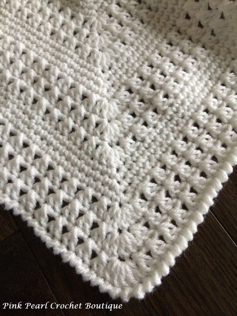 May include: White crochet blanket with a delicate stitch pattern. The blanket has a scalloped edge and is made with a soft, lightweight yarn.