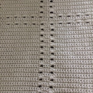May include: A close-up of a white crocheted fabric with a repeating pattern of holes.