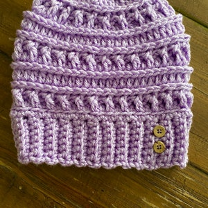 May include: A purple crocheted beanie with two brown buttons.