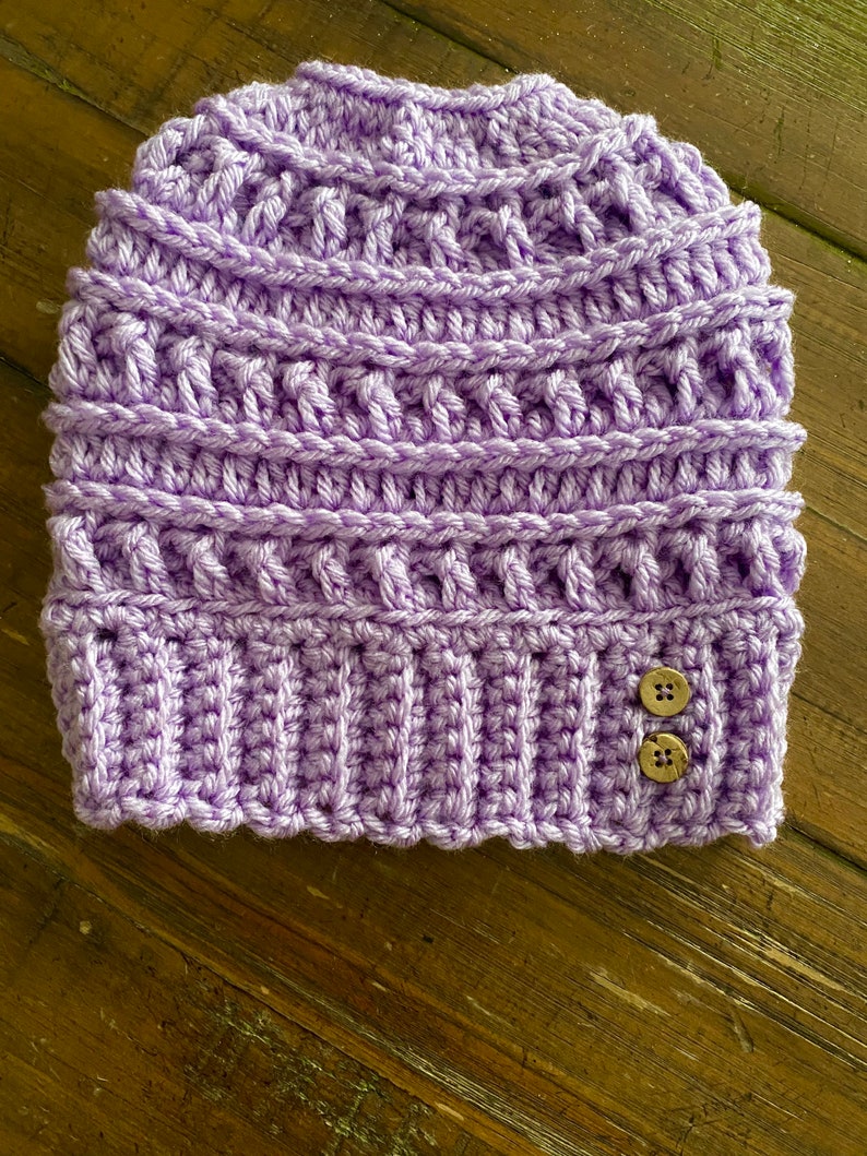 May include: A purple crocheted beanie with two brown buttons.