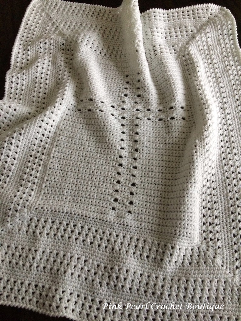 May include: White crochet baby blanket with a cross pattern in the center. The blanket is made with a delicate stitch and has a soft, airy feel.