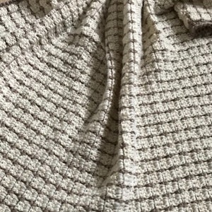 May include: A close-up of a beige and brown crocheted throw blanket with a textured waffle stitch pattern.