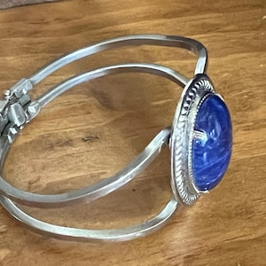 May include: A silver bangle bracelet with a blue oval cabochon stone set in a silver bezel. The stone has a swirling pattern.