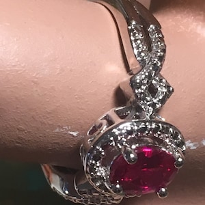 Puede incluir: Un anillo de plata con una gran piedra roja rodeada de piedras peque&ntilde;as transparentes. El anillo tiene una banda retorcida.