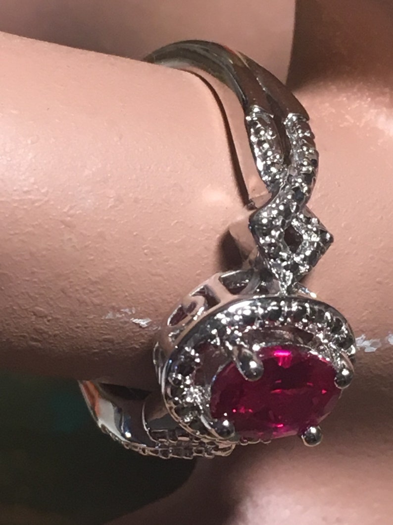 Puede incluir: Un anillo de plata con una gran piedra roja rodeada de piedras peque&ntilde;as transparentes. El anillo tiene una banda retorcida.