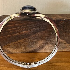 May include: A silver hinged bangle bracelet with a dark blue oval cabochon gemstone set in a silver bezel.