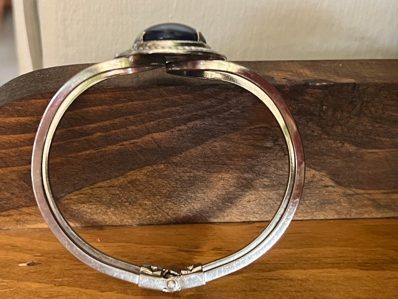 May include: A silver hinged bangle bracelet with a dark blue oval cabochon gemstone set in a silver bezel.