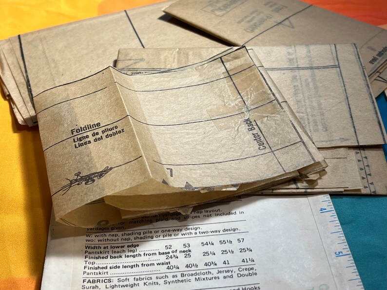 Puede incluir: Un conjunto de piezas de patr&oacute;n de papel marr&oacute;n para coser una prenda. Las piezas del patr&oacute;n tienen l&iacute;neas y marcas para cortar y coser. El texto en las piezas del patr&oacute;n incluye "Foldline", "Ligne de pliure", "Linea del doblez" y "Center Back".