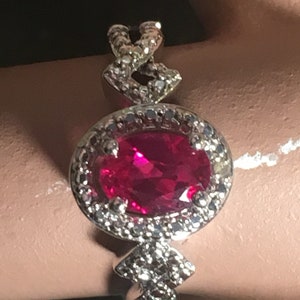 Puede incluir: Un anillo de plata con una gran piedra de rub&iacute; ovalada rodeada de diamantes m&aacute;s peque&ntilde;os. La banda est&aacute; intrincadamente dise&ntilde;ada con un patr&oacute;n trenzado.