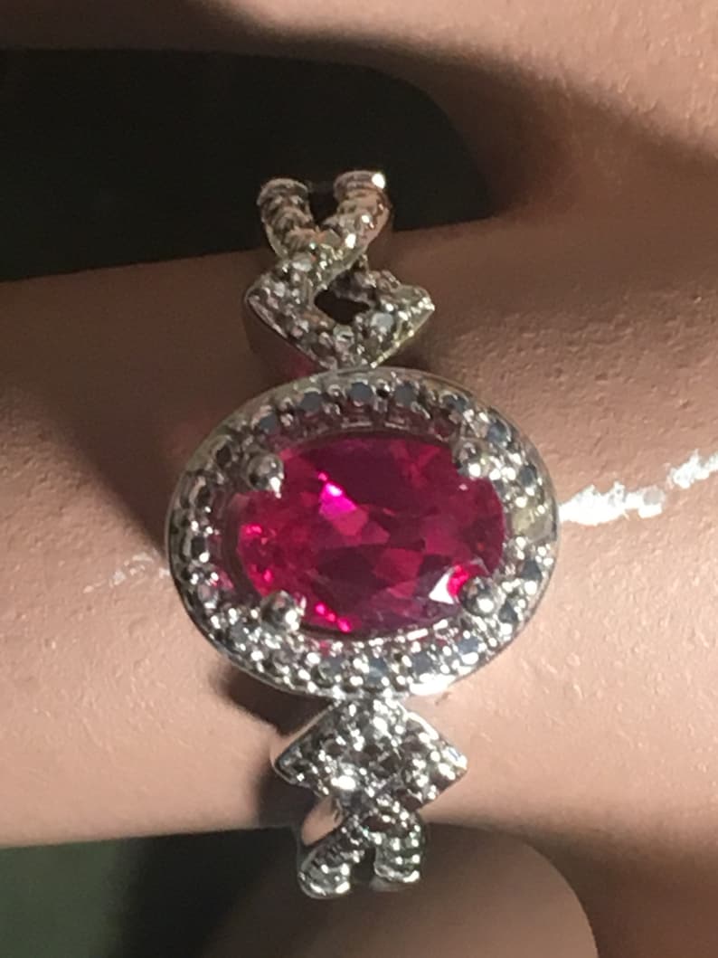 Puede incluir: Un anillo de plata con una gran piedra de rub&iacute; ovalada rodeada de diamantes m&aacute;s peque&ntilde;os. La banda est&aacute; intrincadamente dise&ntilde;ada con un patr&oacute;n trenzado.