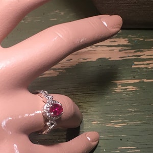 Puede incluir: Un anillo de plata con una piedra ovalada roja rodeada de piedras peque&ntilde;as transparentes.