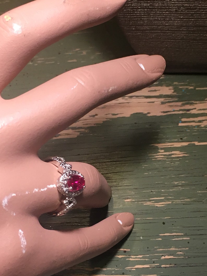 Puede incluir: Un anillo de plata con una piedra ovalada roja rodeada de piedras peque&ntilde;as transparentes.