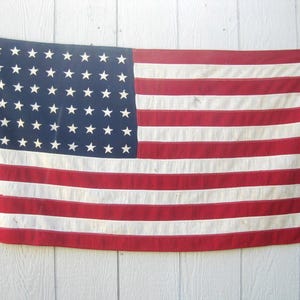 May include: A vintage 48-star American flag featuring a blue canton with white stars arranged in rows and thirteen horizontal red and white stripes. The flag includes a white vertical header strip on the left side with two metal grommets.