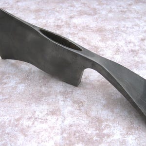 May include: A dark gray axe head with a curved blade and a hole for the handle. The axe head is made of metal and has a slightly textured surface. The overall design is simple and functional.