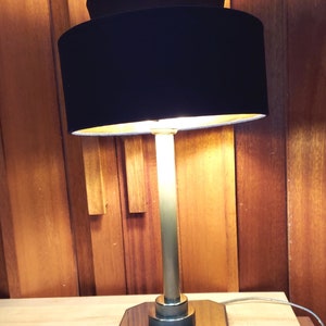 May include: A black velvet lampshade with a gold base and a square metal base. The lamp is turned on and illuminating the room.
