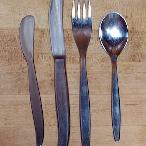 May include: A set of four silver utensils, including a butter knife, a fork, a spoon, and a small knife. The utensils are arranged on a wooden surface.