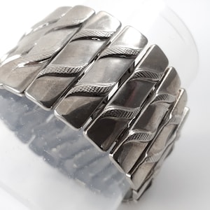 May include: A silver bracelet with a textured, wavy design. The bracelet is made of multiple linked pieces.