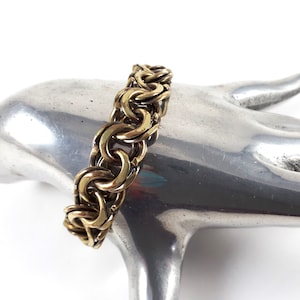 May include: A gold-toned chain bracelet with a woven design. The bracelet is made of interlocking rings.