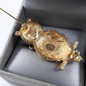 May include: Gold-toned owl brooch with a detailed design and a pin closure. The back of the brooch has the word "MANRICO" engraved on it.