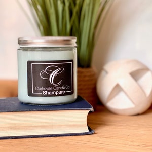 May include: A light blue glass candle jar with a silver lid. The candle is labeled "Clarksville Candle Co. - Shampure" with a stylized letter "C" logo.