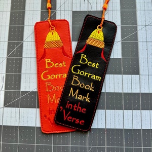 May include: Two red and black leather bookmarks with orange tassels. The bookmarks feature an embroidered image of a yellow and orange hat with the text "Best Gorram Book Mark in the Verse".