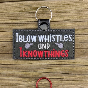 May include: Black leather keychain with a red and white embroidered design. The text reads "I blow whistles and I know things".