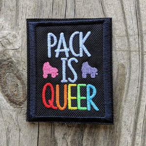 May include: Black embroidered patch with the text "Pack is Queer" in rainbow colors. Two roller skate silhouettes are between the words "Pack" and "Queer".