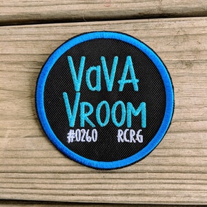 May include: A black and blue round patch with the text "VAVA VROOM" in blue and "#0260 RCRG" in white.