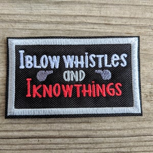 Puede incluir: Parche bordado negro con costuras blancas. El parche dice "I blow whistles and I know things" con un gráfico de silbato a cada lado del texto.