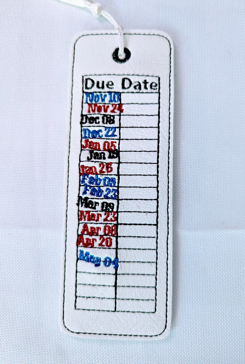 May include: White leather bookmark with a stitched grid and embroidered text that reads "Due Date" and a list of dates in blue and red. The dates are: Nov 10, Nov 24, Dec 08, Dec 22, Jan 05, Jan 15, Jan 26, Feb 09, Feb 23, Mar 08, Mar 23, Apr 08, Apr 20, May 04.