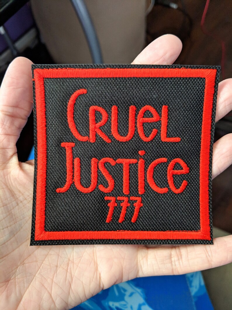 Może przedstawiać: Czarna naszywka haftowana z czerwonymi szwami. Naszywka zawiera napis "Cruel Justice 777".