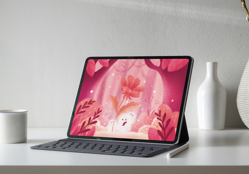 Puede incluir: Una tableta digital que muestra una ilustraci&oacute;n caprichosa de una flor y dos figuras blancas en un bosque rosa. La tableta est&aacute; sobre una funda de teclado con un l&aacute;piz &oacute;ptico, junto a una taza y jarrones blancos.