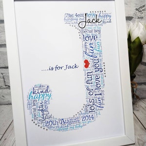 May include: A framed print with a blue and white word cloud in the shape of a letter J. The word cloud includes words like "love", "happy", "fun", "special boy", "7lbs 4ozs", "20th August 2014", and "Jack".