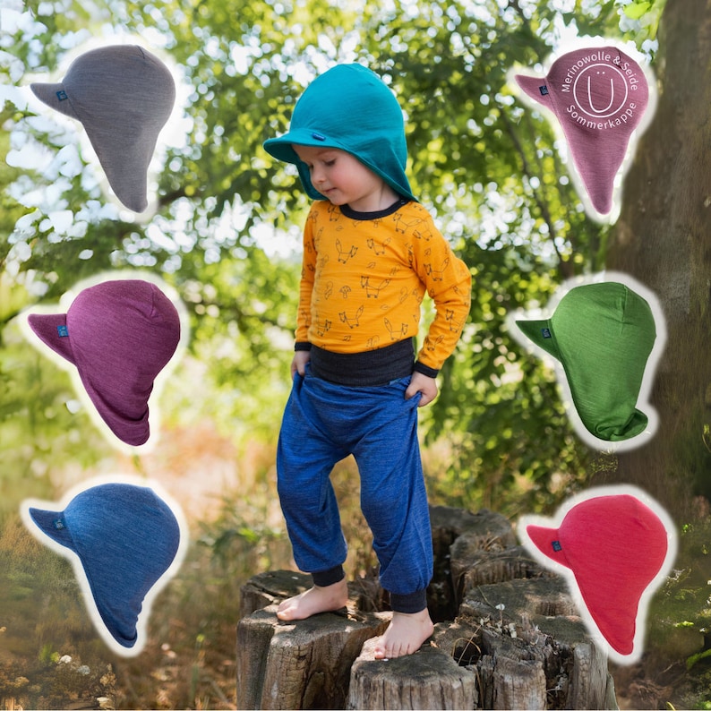 May include: A child wearing a teal hooded sun hat with a brim and a yellow long-sleeved shirt with a fox print. The child is standing on a tree stump. There are six different colored sun hats with brims and hoods around the child. The hats are in the colors teal, gray, purple, green, blue, and red.