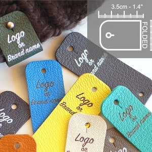 Peut inclure: Assortiment d'étiquettes en cuir de différentes couleurs, chacune avec un trou perforé en haut. Les étiquettes sont rectangulaires et présentent le texte "Logo ou Nom de la marque" en lettres blanches. Les étiquettes mesurent environ 3,5 cm sur 2,5 cm une fois pliées.