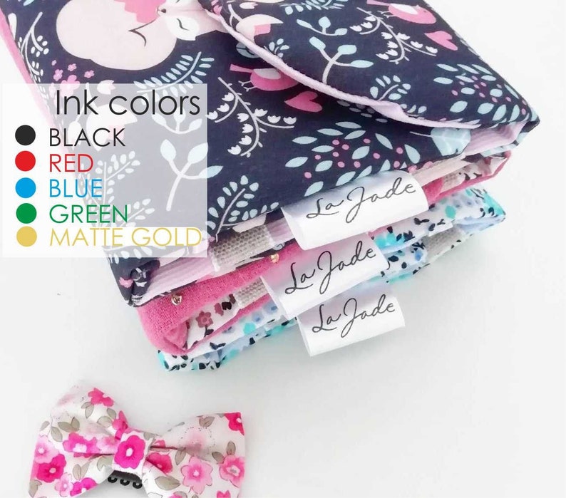 K&ouml;nnte beinhalten: Ein Stapel Stoffquadrate mit Blumenmustern in Rosa, Blau und Wei&szlig;. Die Stoffquadrate haben wei&szlig;e Etiketten mit dem Text "La Jade" in schwarzer Schrift. Die Stoffquadrate sind auf einer wei&szlig;en Oberfl&auml;che gestapelt. Rechts unten im Bild befindet sich eine kleine rosa-wei&szlig;e Blumen Schleife.