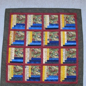 May include: A quilt with a patchwork design featuring squares of blue, yellow, and green fabric. The squares are arranged in a grid pattern and are bordered by a dark brown fabric.