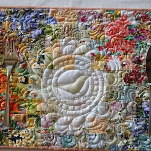 Könnte beinhalten: Ein gequilteter Platzdeckchen mit einem Blumenmuster und einer weißen Mitte mit einem gesteppten Design. Eine silberne Gabel und ein Buttermesser liegen auf dem Platzdeckchen.