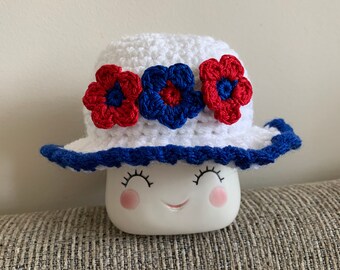 May include: White crocheted sun hat with blue and red flower embellishments.