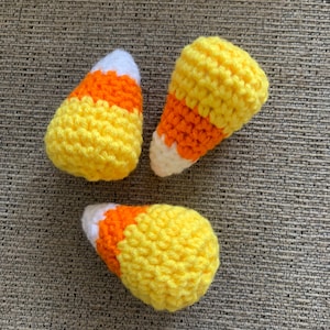 May include: Three crocheted candy corn ornaments in yellow, orange, and white.