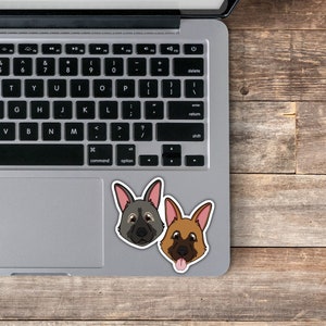 Op de afbeelding: Twee cartoon-hondensticker op een zilveren laptop. De hond links heeft grijze vacht en bruine ogen. De hond rechts heeft bruine vacht en bruine ogen. Beide honden hebben roze neuzen en tongen.