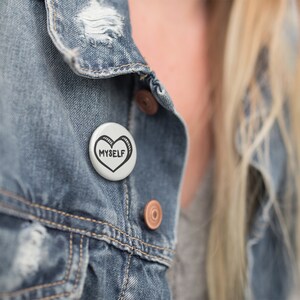May include: A white button with a black heart and the text "MYSELF" on a denim jacket.