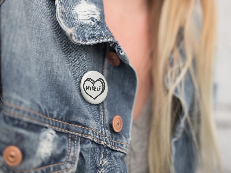 May include: A white button with a black heart and the text "MYSELF" on a denim jacket.