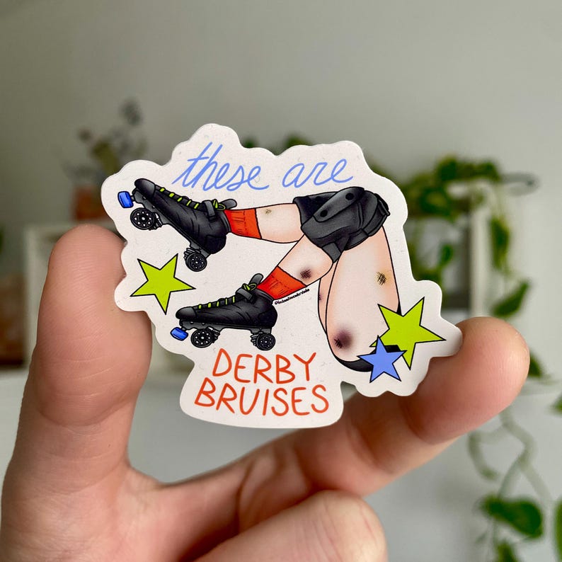 May include: A sticker featuring a cartoon illustration of legs with roller skates and bruises. The text "these are" is written in blue script above the legs, and "DERBY BRUISES" is written in red block letters below. The sticker has a white background with yellow and blue star accents.