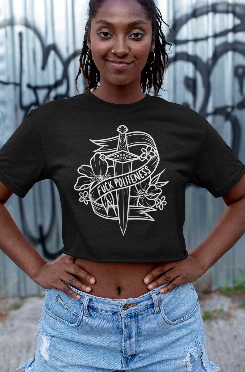 Op de afbeelding: Zwart getailleerd T-shirt met een witte afbeelding van een zwaard met bloemen en een banner met de tekst "F*CK POLITENESS".