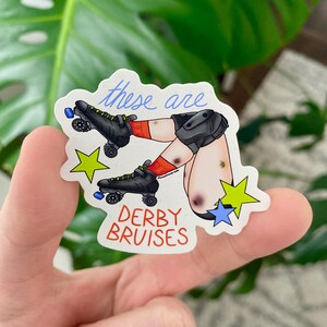 May include: A sticker featuring an illustration of legs with roller skates and bruises. The text "these are" is written in blue script above the legs, and "DERBY BRUISES" is written in red block letters below. Green and blue stars are also included.