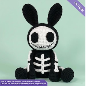 Puede incluir: Un juguete de conejo de ganchillo en blanco y negro con un diseño de esqueleto. El conejo tiene grandes orejas negras, una cabeza blanca con ojos negros y una boca cosida. El cuerpo presenta un diseño de esqueleto blanco sobre un fondo negro. La imagen incluye el texto "PATTERN".