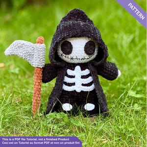 Könnte beinhalten: Gehäkelte Sensenmann-Puppe mit schwarzem Kapuzenmantel, weißem Totenkopfgesicht und Skelettmuster auf der Brust. Sie hält eine graue Sense mit braunem Griff. Der Text auf dem Bild lautet "PATTERN".