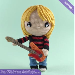 May include: A crocheted doll with yellow hair, black and red striped shirt, blue jeans, and black shoes, holding an orange and brown guitar. The doll has large black eyes. Text on the image reads "PATTERN" and "This is a PDF file Tutorial, not a finished Product".