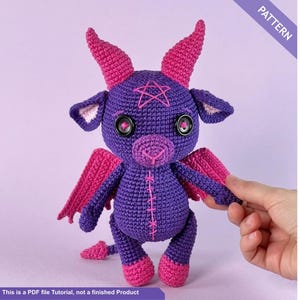 Könnte beinhalten: Ein gehäkeltes lila-rosa Plüschtier mit Hörnern, Flügeln und einem Pentagramm auf dem Kopf. Das Spielzeug hat schwarze Knopfaugen und rosa Akzente. Der Text "PATTERN" und "This is a PDF file Tutorial, not a finished Product" sind enthalten.